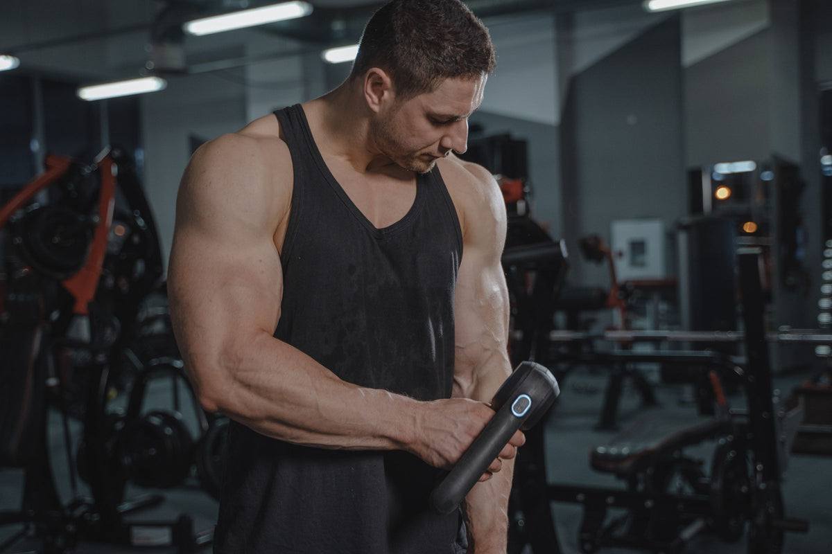 Athlete using a massage gun on his arm after training