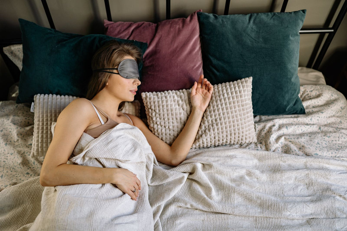 Woman sleeping with an eye mask on teal pillows